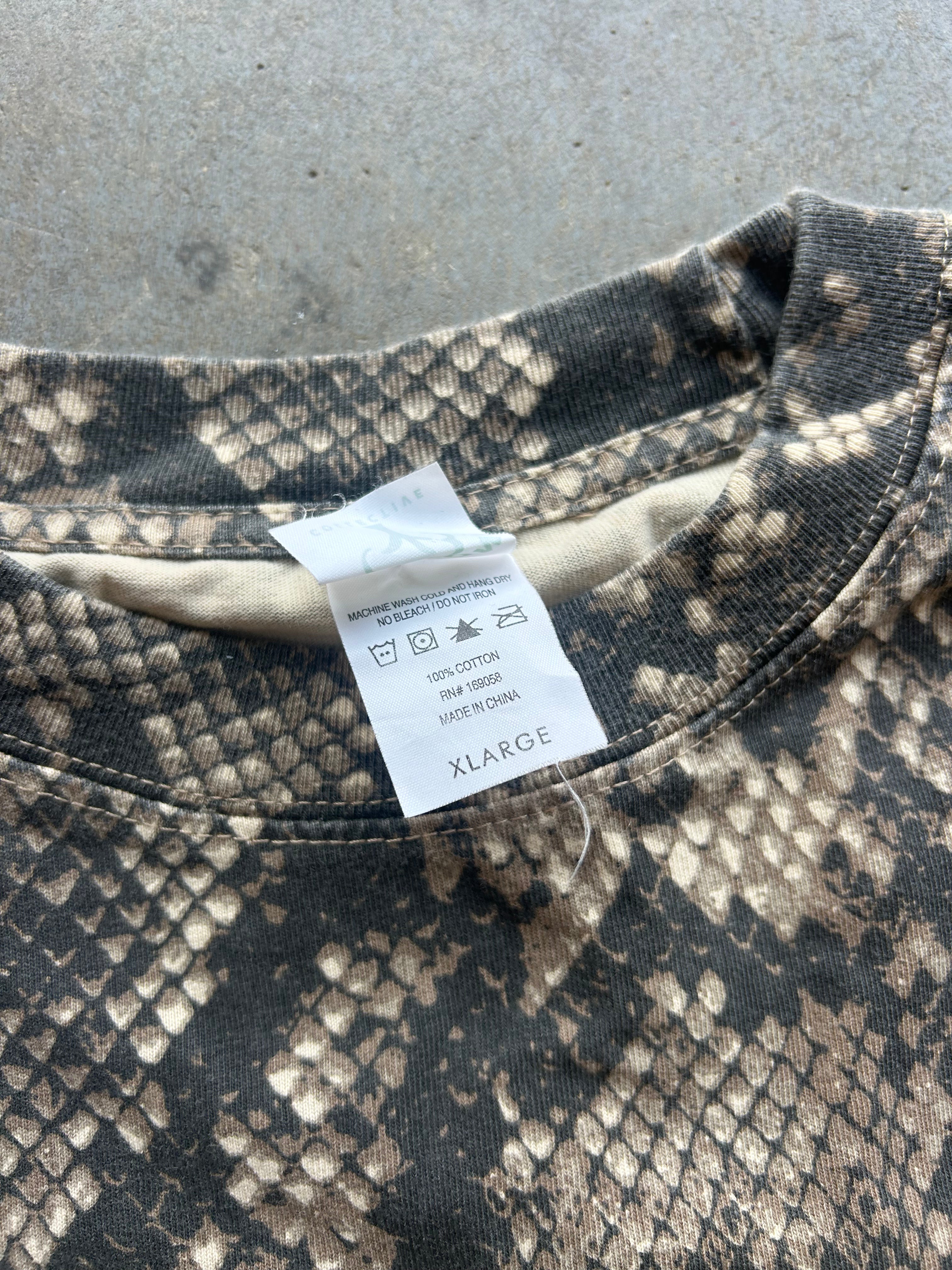 Close-up of a crewneck sweatshirt with a dark gray and beige snakeskin pattern, featuring a white size tag that reads XLARGE.