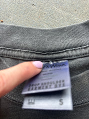 Close-up of a gray ribbed garment neck with a finger pointing at a sewn-in label that reads 'FA WOK' and 'DROP SHOULDER GARNMENT DYE'.