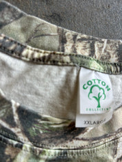 Close-up of a camouflage-patterned garment neck with a white sewn-in label reading COTTON COLLECTIVE and XXLARGE.