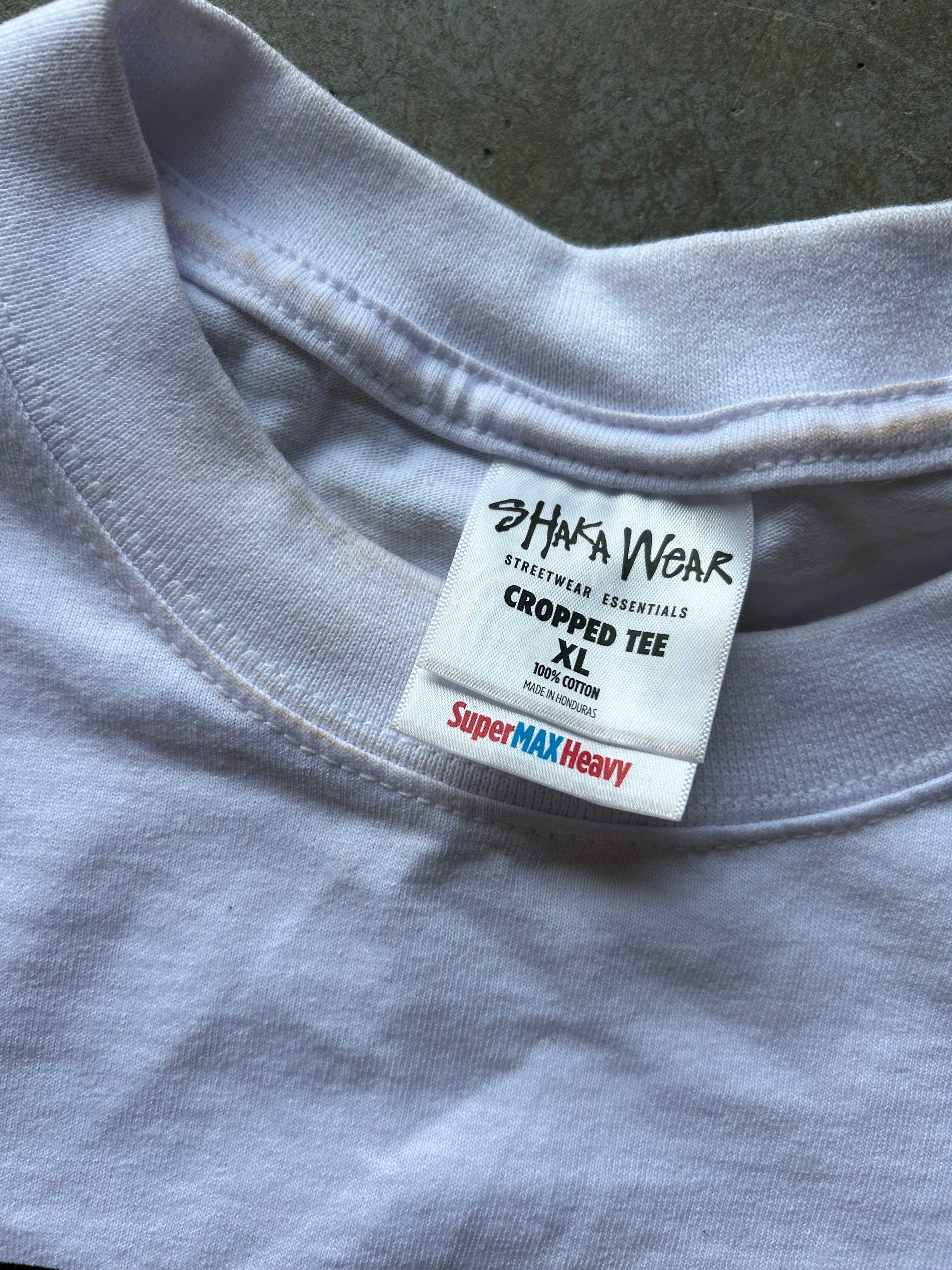 Close-up of a light gray cropped t-shirt showing the inner neck label which reads 'SHAKA WEAR' and 'SuperMAX Heavy'.