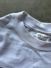 Close-up of a white crewneck t-shirt showing the inner neck label which reads 'SHAKA WEAR'.