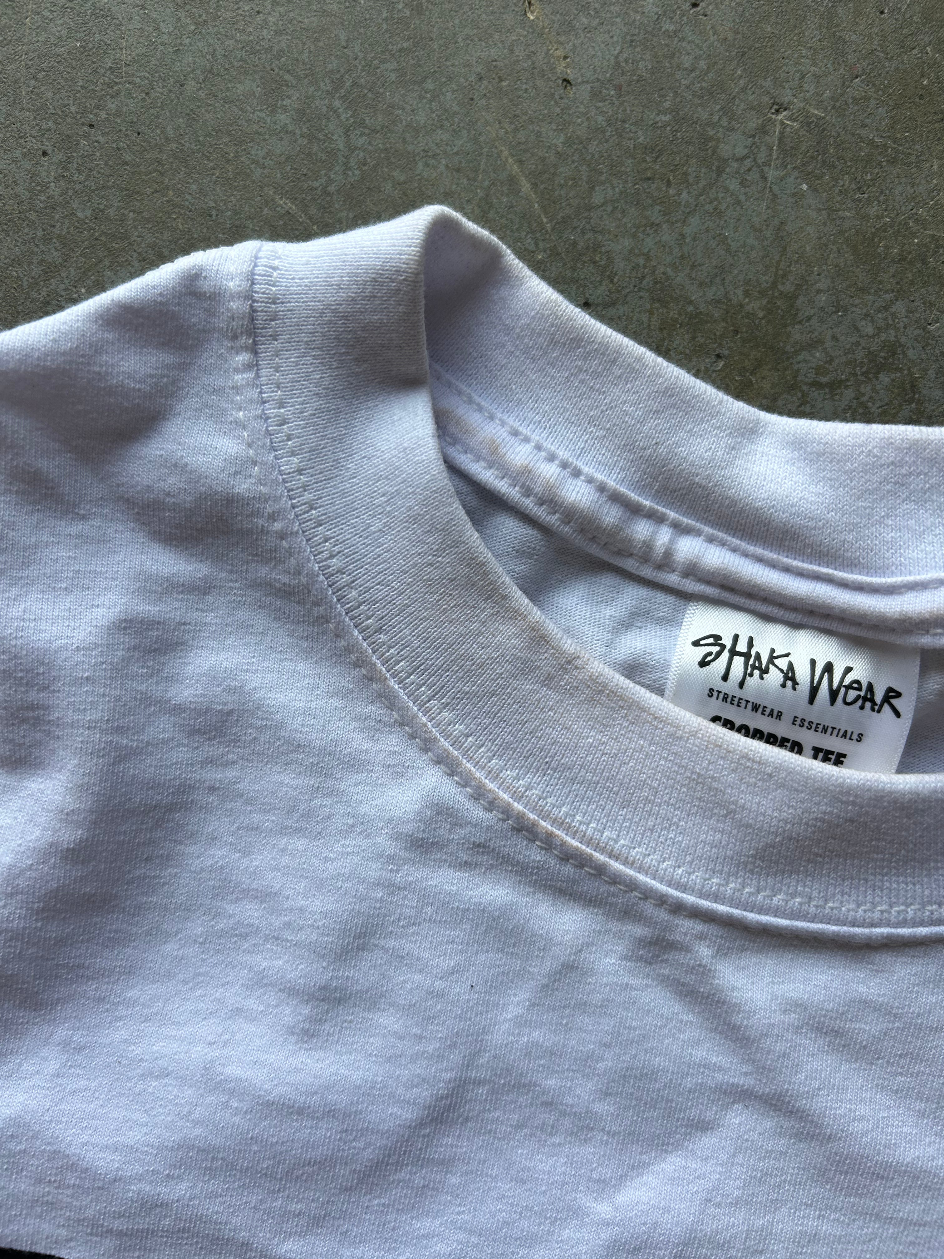 Close-up of a white crewneck t-shirt showing the inner neck label which reads 'SHAKA WEAR'.