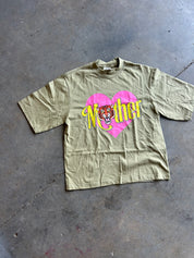 An olive green short-sleeve t-shirt with a graphic print of a pink heart, yellow 'Mother' text, and a tiger face, laid flat on a gray concrete floor.