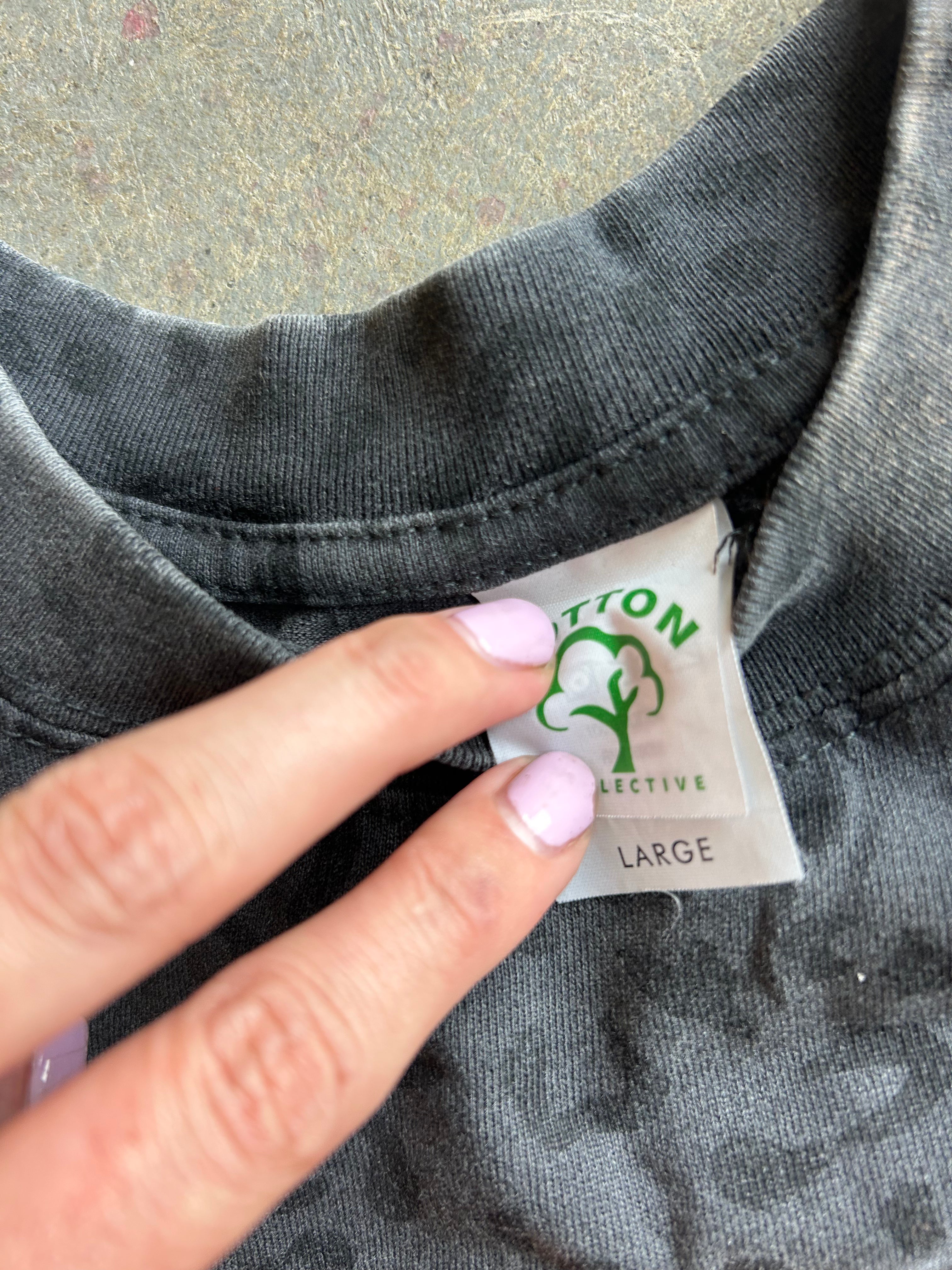 Close-up of a dark gray t-shirt collar showing a sewn-in label for Cotton Collective, with a hand pointing to the label.