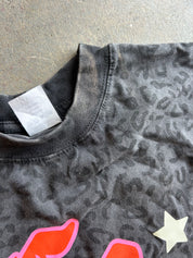 Close-up of a dark gray washed t-shirt with a subtle leopard print pattern, featuring a white neck label and a cream star graphic.