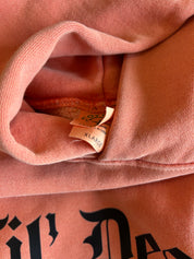 Close-up of a dusty pink sweatshirt showing the interior neck tag which reads 'SILK' and 'LARGE', with black gothic lettering partially visible on the front.
