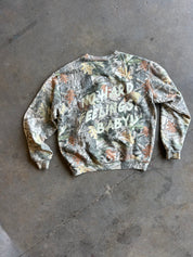 A camouflage crewneck sweatshirt with the text 'I'NO HARD FEELINGS BABY!' printed in white across the chest, laid flat on a gray concrete floor.