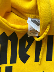 Close-up of a bright yellow hoodie showing the inner neck tag, drawstring, and part of a large black graphic print.