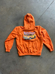 An orange hooded sweatshirt with a 'Motherhood Night Out' graphic featuring a yellow car, laid flat on a gray concrete floor.