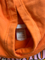 Close-up of an orange cotton garment showing the inner neck label with text reading '100% COTTON' and 'MADE IN CHINA' alongside care symbols and size 'L'.