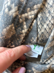 Close-up of a snakeskin-patterned garment with a finger pointing to a white brand label that reads 'Collective London Fashion' and 'LARGE'.