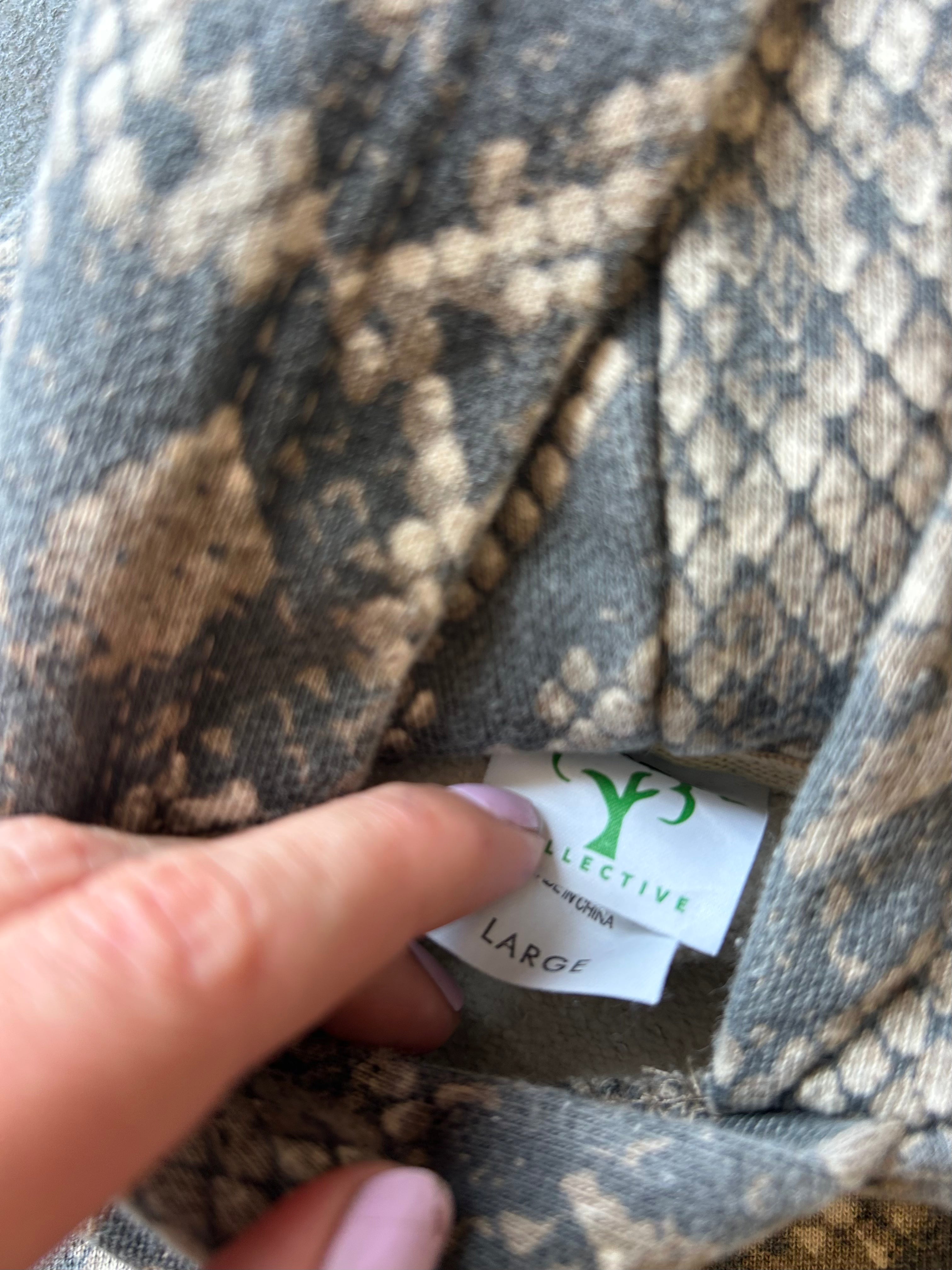 Close-up of a snakeskin-patterned garment with a finger pointing to a white brand label that reads 'Collective London Fashion' and 'LARGE'.
