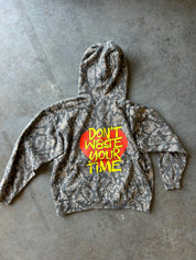 A gray and black snakeskin-patterned hoodie with a red heart graphic and yellow text reading 'DON'T WASTE YOUR TIME' on the back, laid flat on a gray concrete floor.