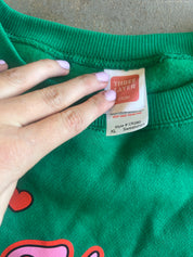 Close-up of a green sweatshirt neck label being held by a hand with light purple nail polish. The label reads THREE LAYER and shows size XL.