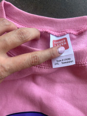 A close-up of a pink sweatshirt showing the inner neck label, which reads 'THREE LAYER' and 'Style # CR280 2XL Sweatshirt'. A hand with light pink nail polish is holding the collar open to display the tag.