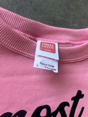 Close-up of a pink crewneck sweatshirt showing the inner neck label with 'THREE LAYER' branding and size information, with part of a black graphic print visible at the bottom.