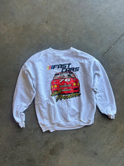 A white long-sleeve crewneck sweatshirt featuring a red race car graphic and the text 'FAST CARS' and 'for Freedom' on the front, laid flat on a gray concrete floor.