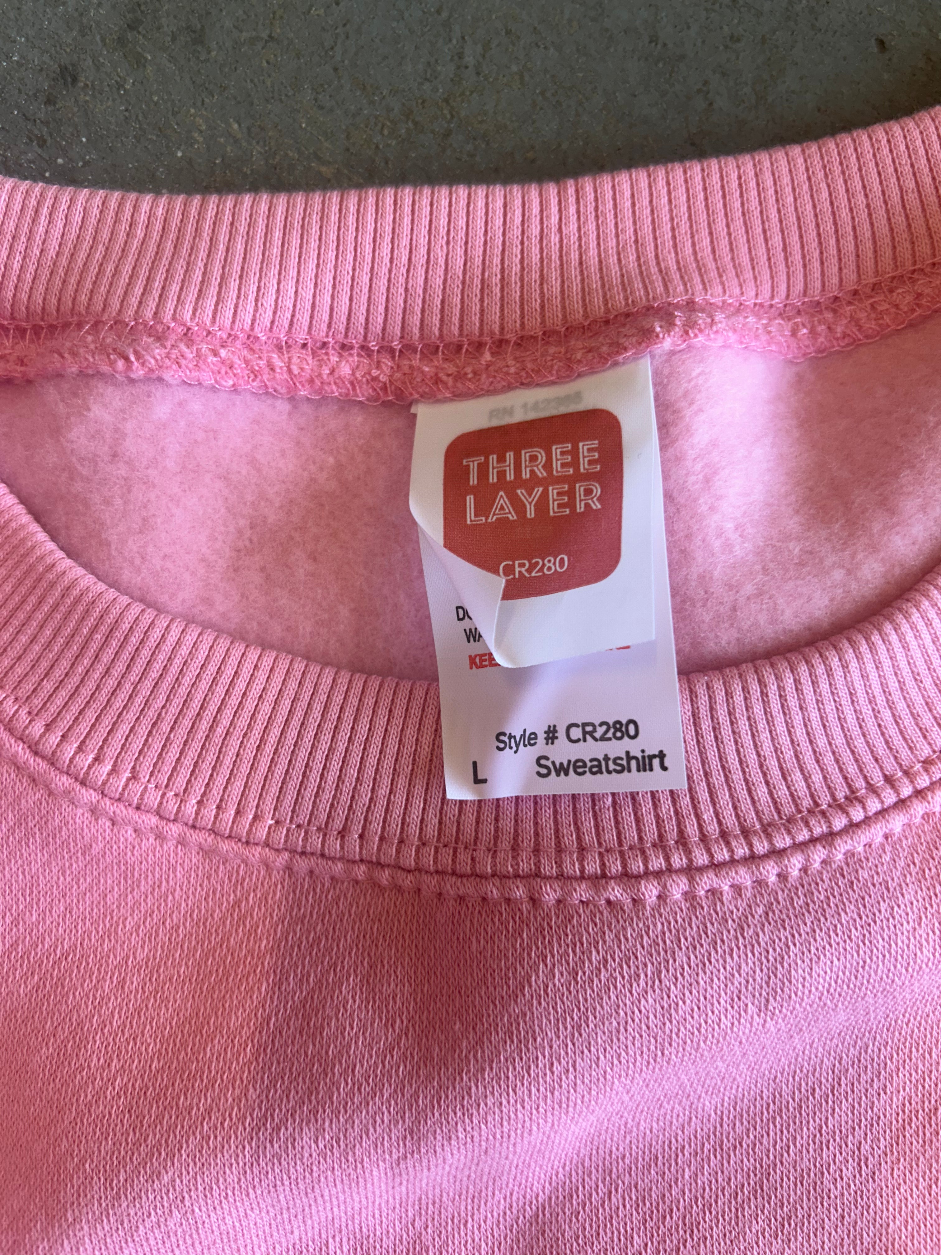 Close-up of a pink crewneck sweatshirt showing the inner neck label which reads 'THREE LAYER' and 'Sweatshirt'.