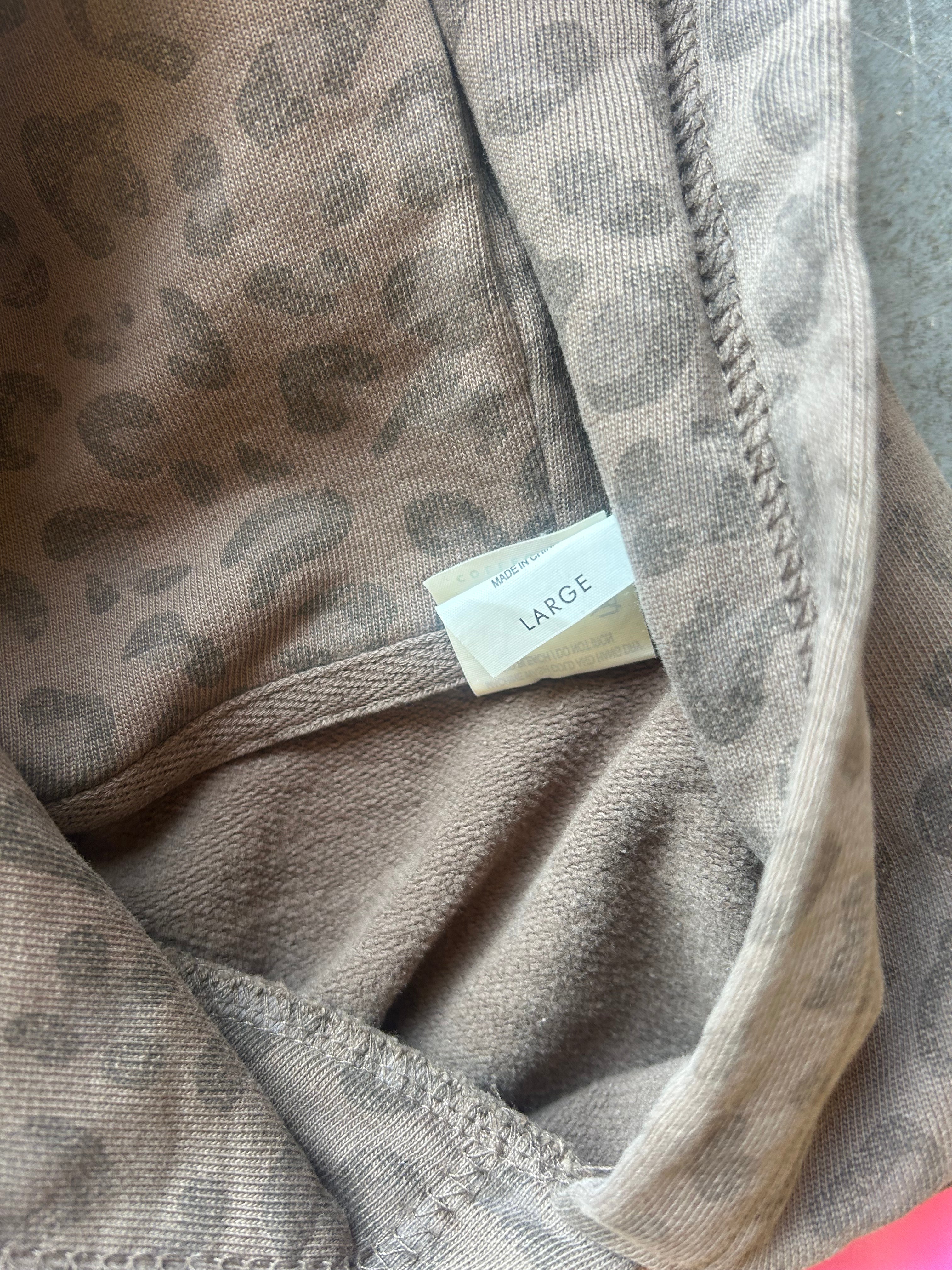 Close-up of a leopard print fabric garment in taupe and brown, showing the interior neckline with a small size tag reading LARGE.