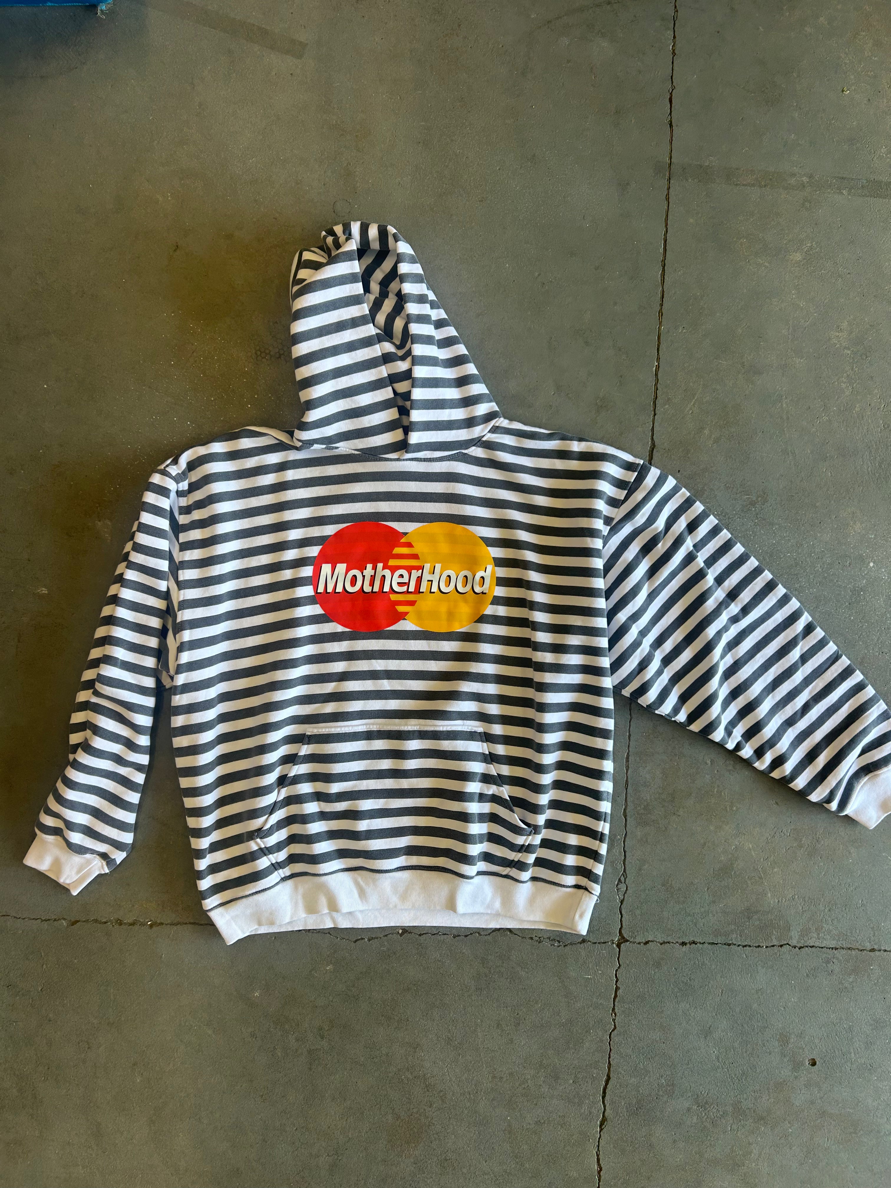 A black and white horizontally striped hoodie with a 'MotherHood' graphic printed on the chest, laid flat on a gray concrete floor.