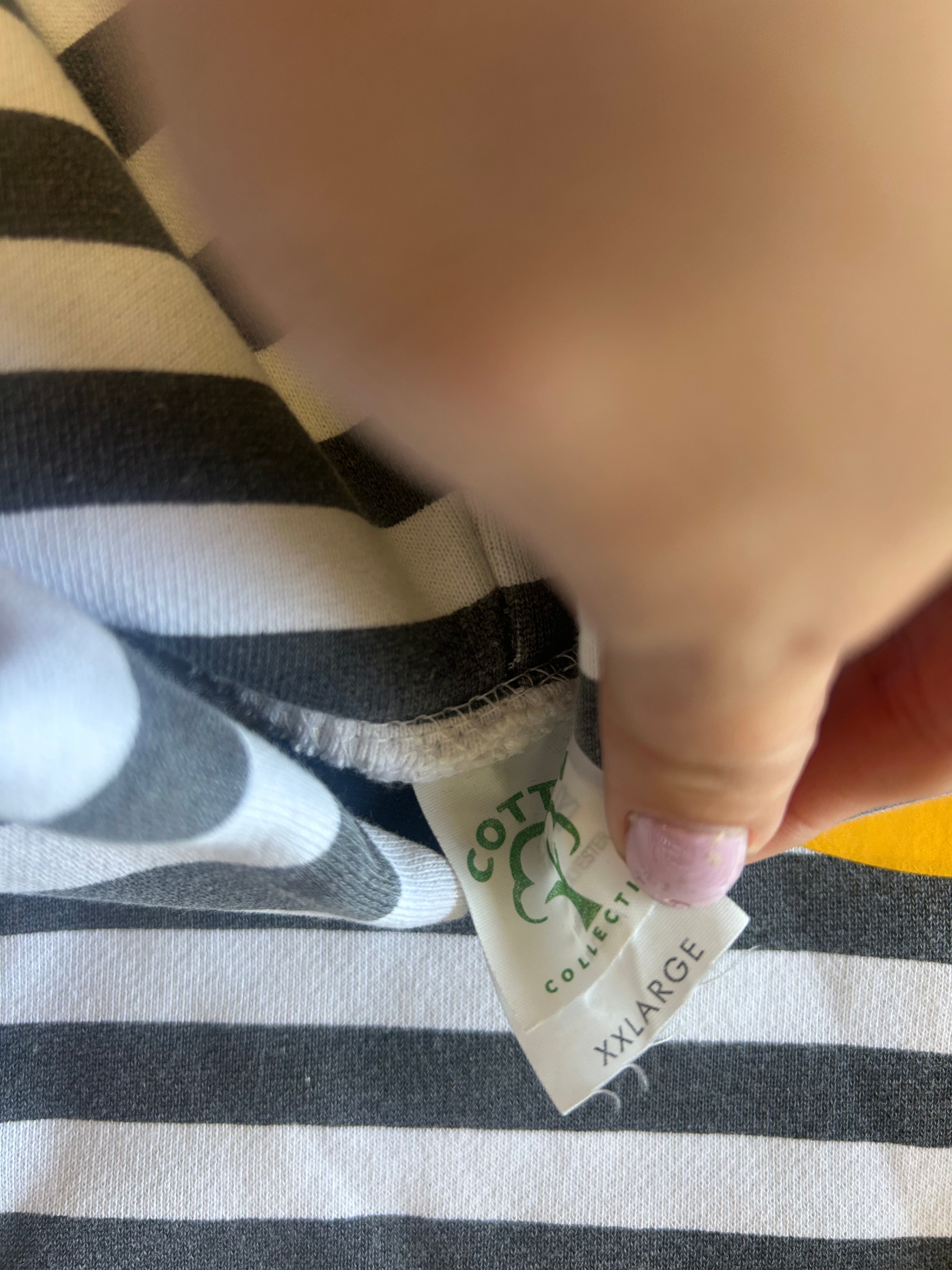 A close-up of a hand holding a cotton label for a black and white striped garment, with the brand name 'COTTON COLLECTION' visible on the tag.