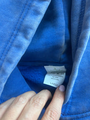 Close-up of a blue fleece-lined garment opening showing a sewn-in size tag labeled LARGE, with a hand pointing to the tag.