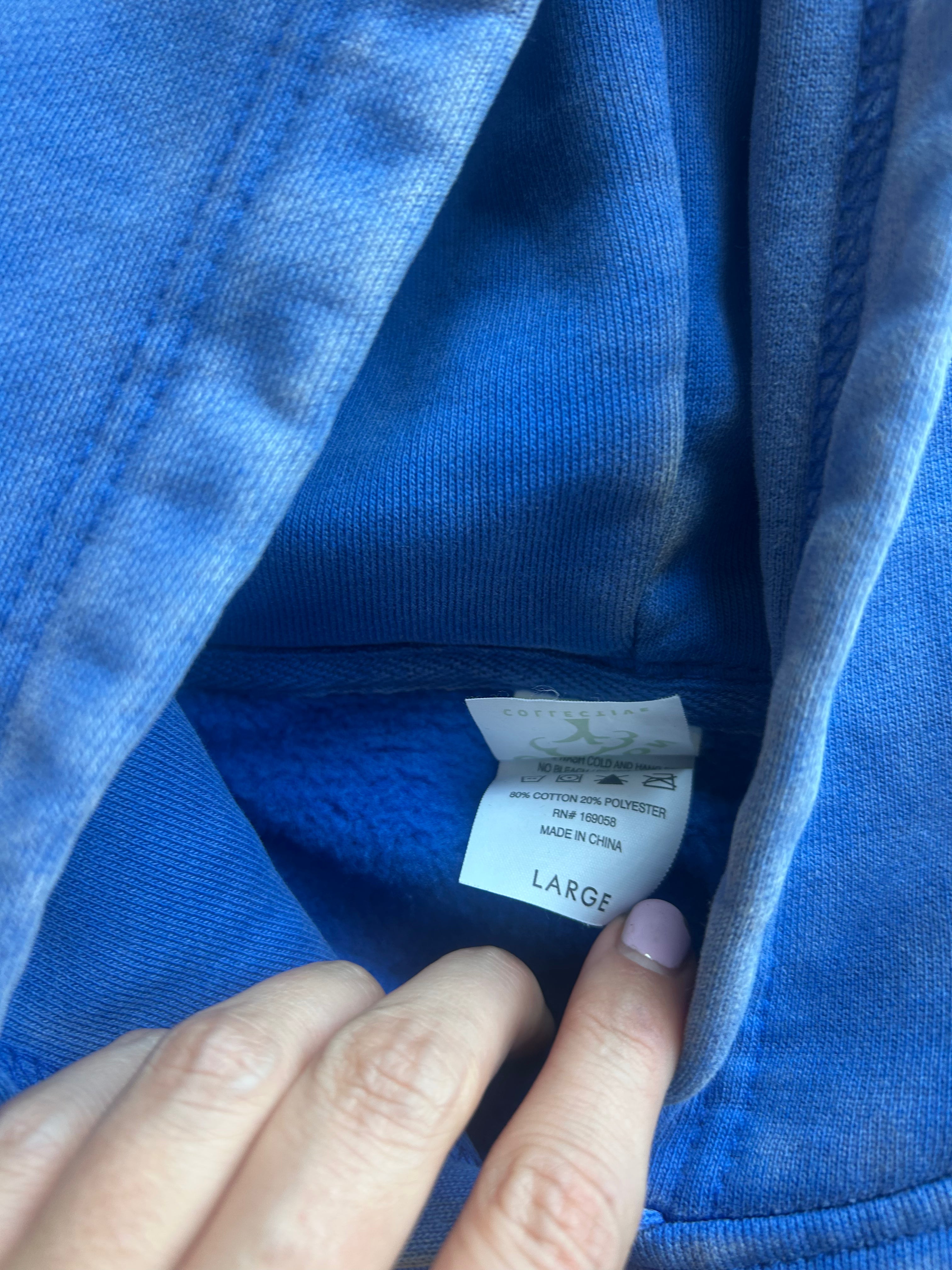 Close-up of a blue fleece-lined garment opening showing a sewn-in size tag labeled LARGE, with a hand pointing to the tag.