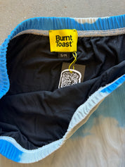 Close-up of the inside waistband of Burnt Toast sweatpants, showing a bright blue and white tie-dye pattern, a black interior lining, and a yellow brand tag