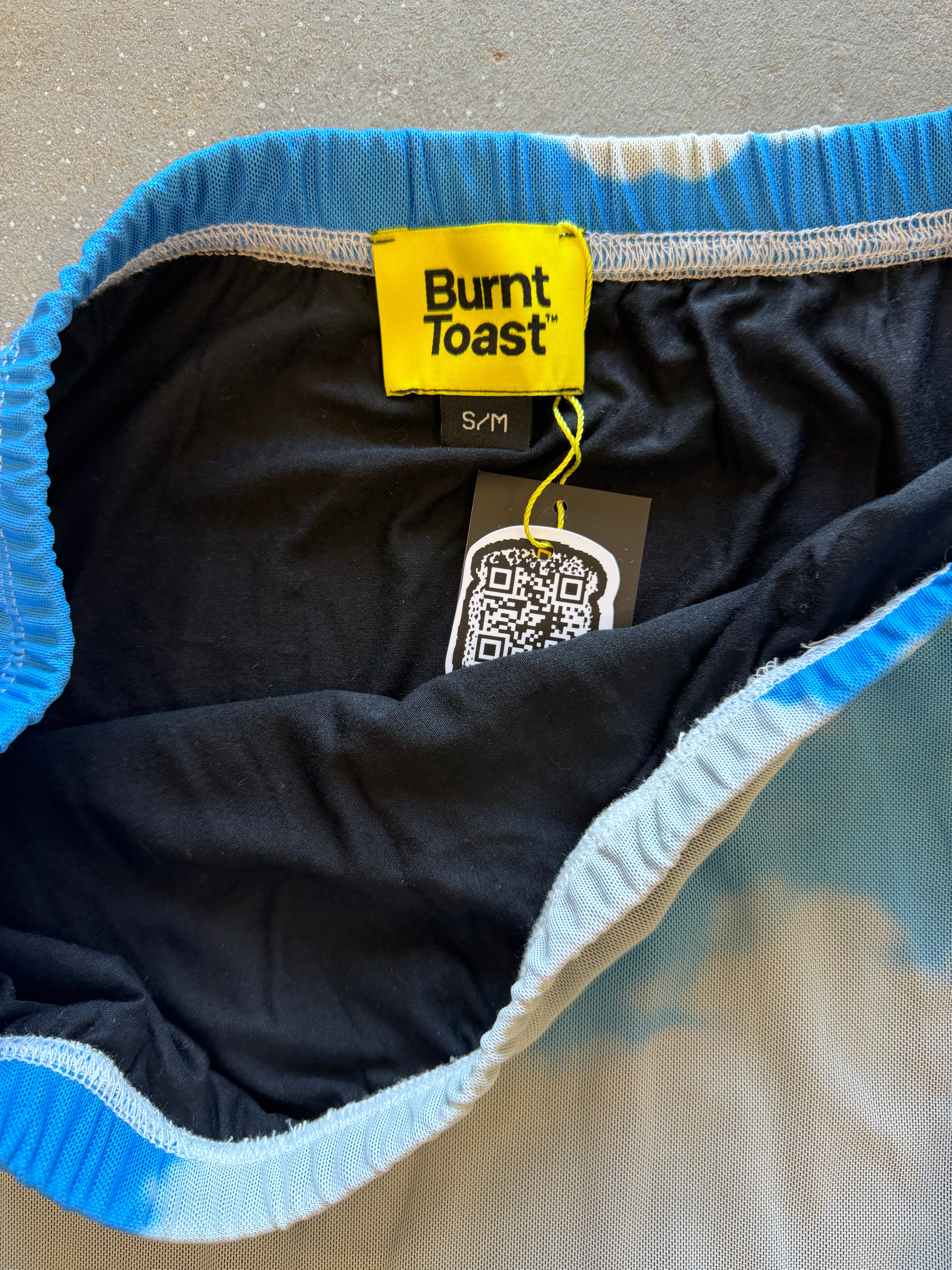 Close-up of the inside waistband of Burnt Toast sweatpants, showing a bright blue and white tie-dye pattern, a black interior lining, and a yellow brand tag