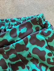 Close-up of a pair of shorts with an elastic waistband, featuring a bold green and brown abstract pattern