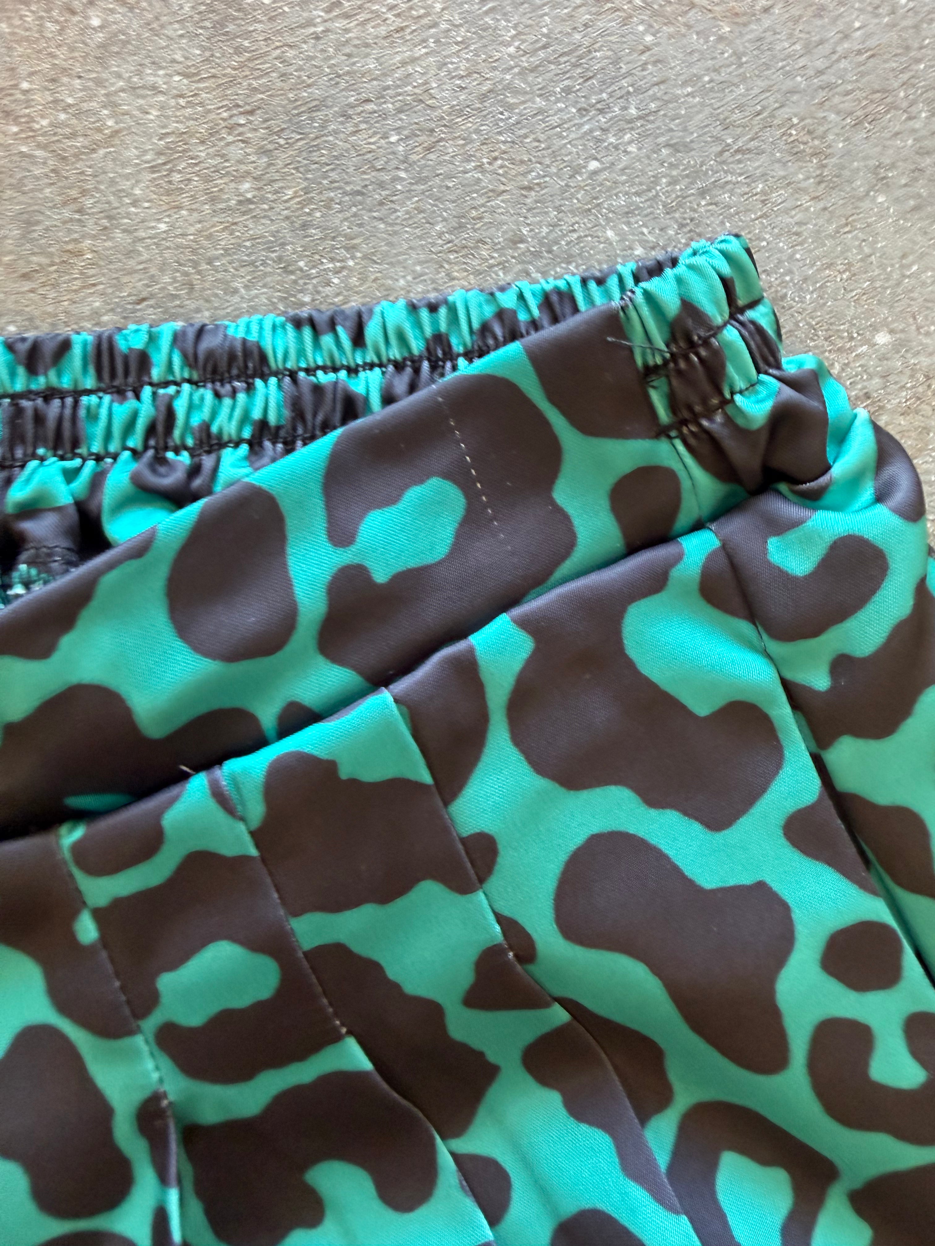 Close-up of a pair of shorts with an elastic waistband, featuring a bold green and brown abstract pattern