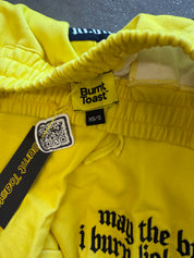 Close-up of bright yellow pants with 'Burnt Toast' branding, featuring gothic text on the front and a black elasticated waistband
