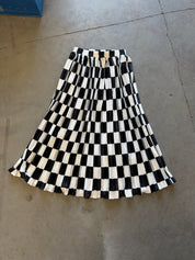 A pleated A-line skirt with a bold black and off-white checkerboard pattern, laid flat on a concrete floor