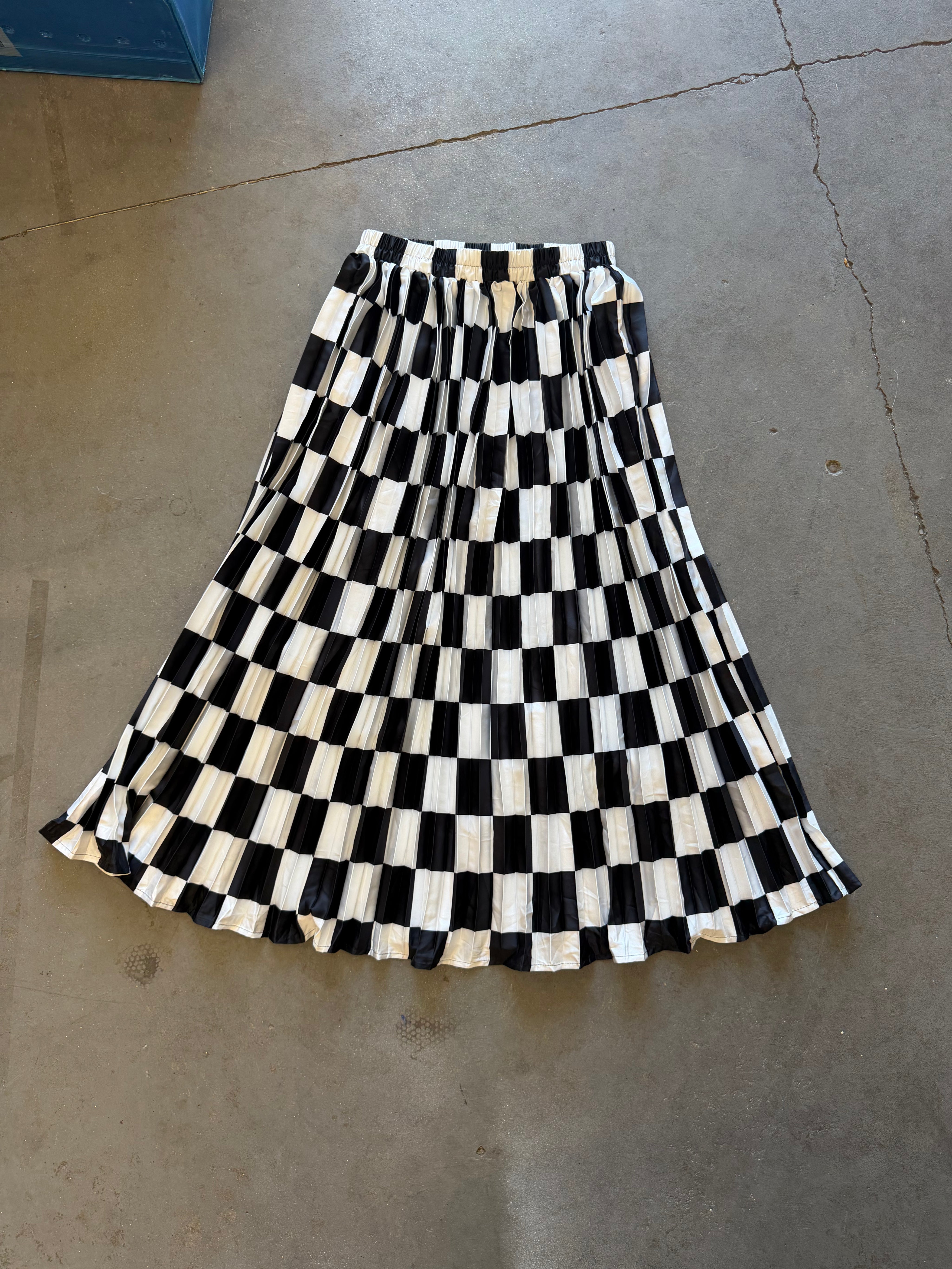 A black and white checkered pleated midi skirt laid flat on a concrete floor