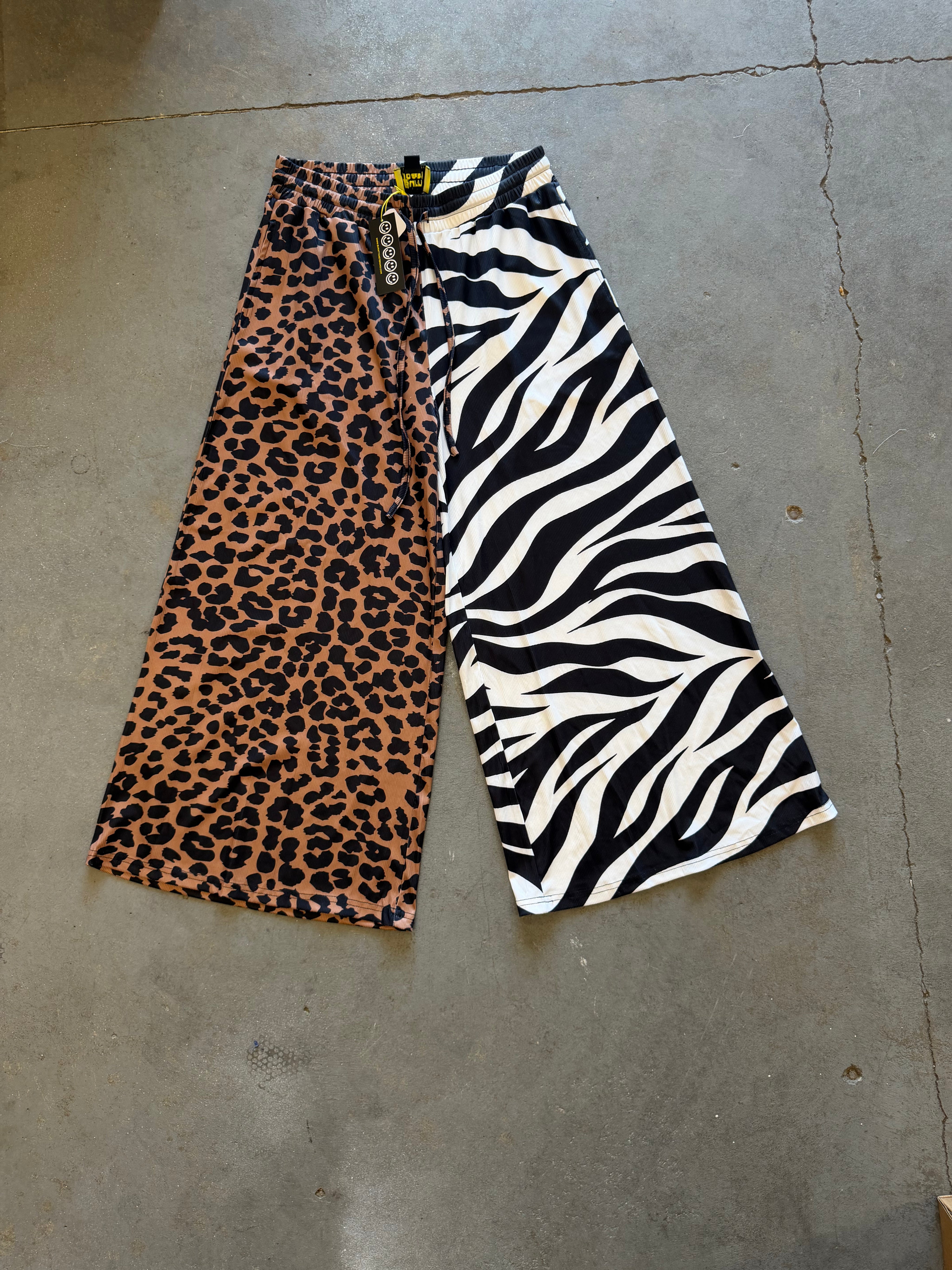 Wide-leg cropped pants laid flat on a concrete floor, featuring a split design with a brown leopard print side and a black and white zebra print side
