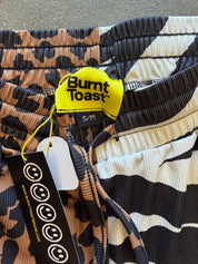 Close-up of Burnt Toast drawstring shorts with a mixed animal print pattern in black, beige, and brown, featuring a bright yellow brand tag and a black hangtag