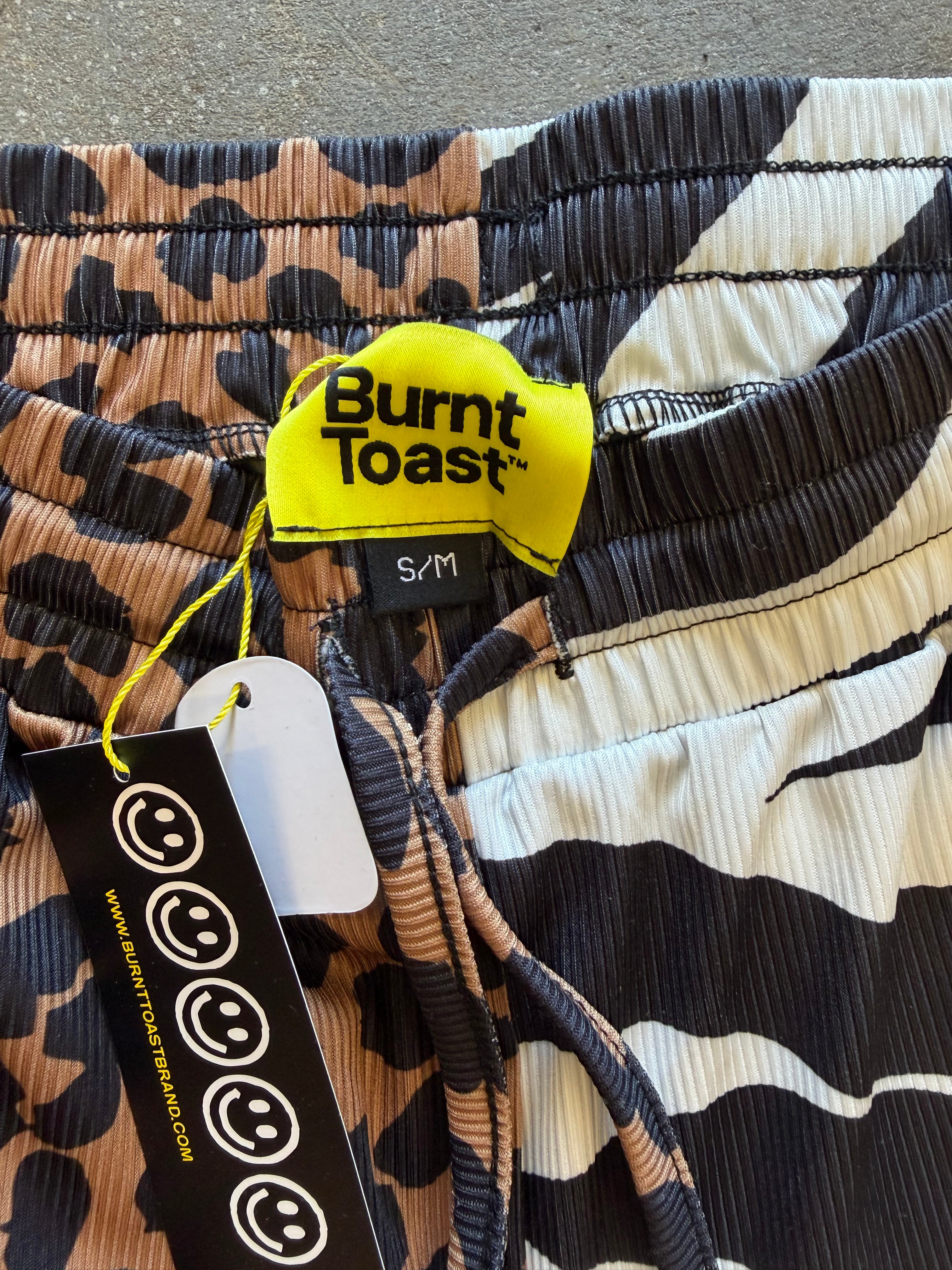Close-up of Burnt Toast drawstring shorts with a mixed animal print pattern in black, beige, and brown, featuring a bright yellow brand tag and a black hangtag