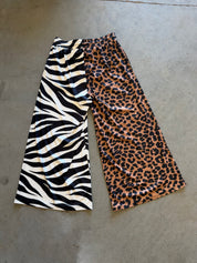 Wide-leg cropped pants laid flat on a concrete floor, featuring a split design with a black and white zebra print on the left leg and a brown, black, and beige leopard print on the right leg