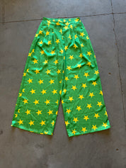 Green wide-leg cropped pants with an all-over yellow star pattern, laid flat on a gray concrete floor