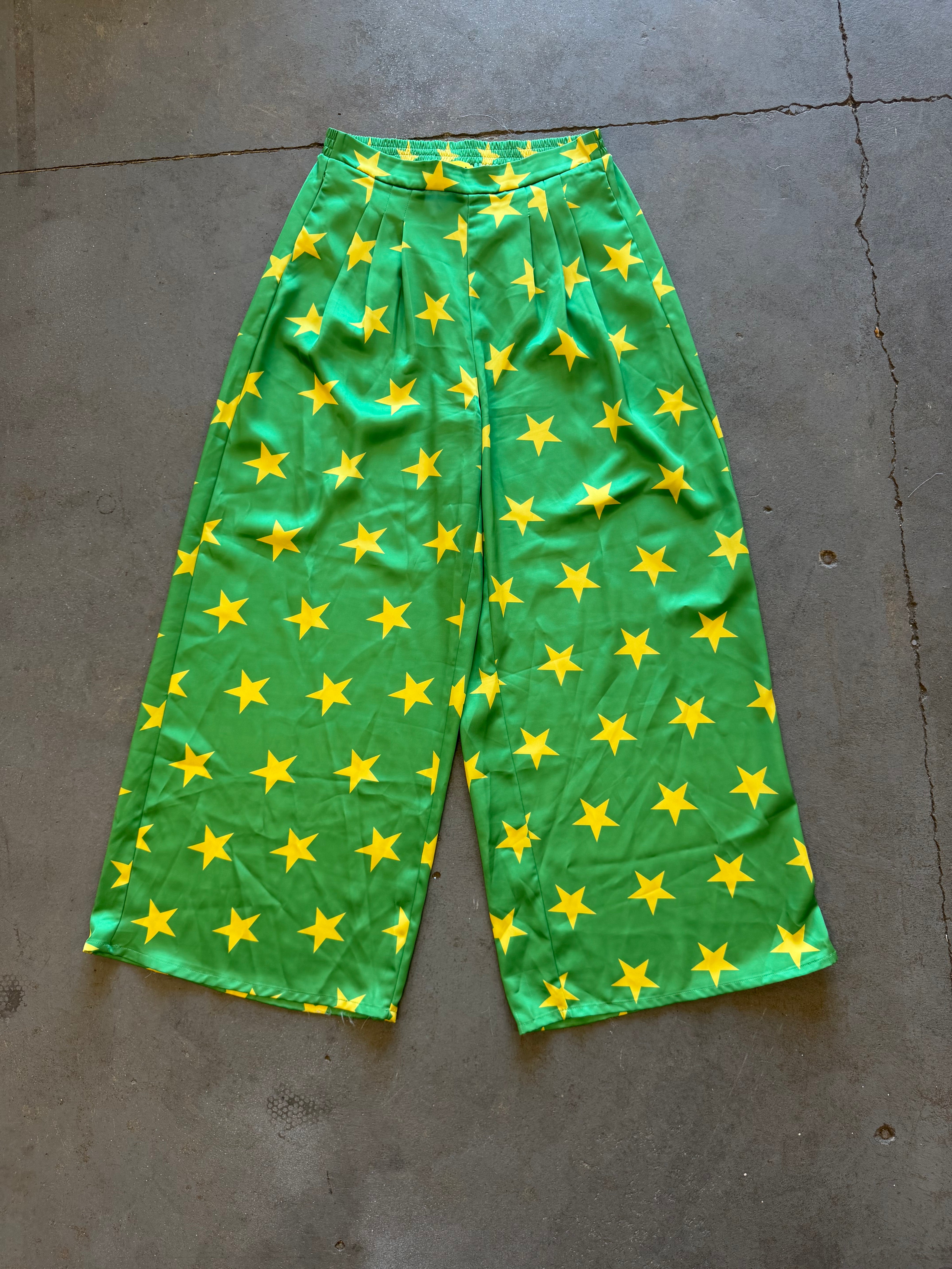Green wide-leg cropped pants with an all-over yellow star pattern, laid flat on a gray concrete floor