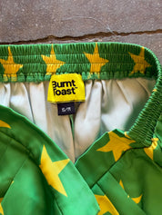 Close-up of a green quilted garment with a yellow star pattern, showing the elastic waistband with a yellow Burnt Toast brand label and an S/M size tag