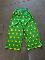 Green wide-leg pants with an all-over yellow star pattern, laid flat on a gray concrete floor