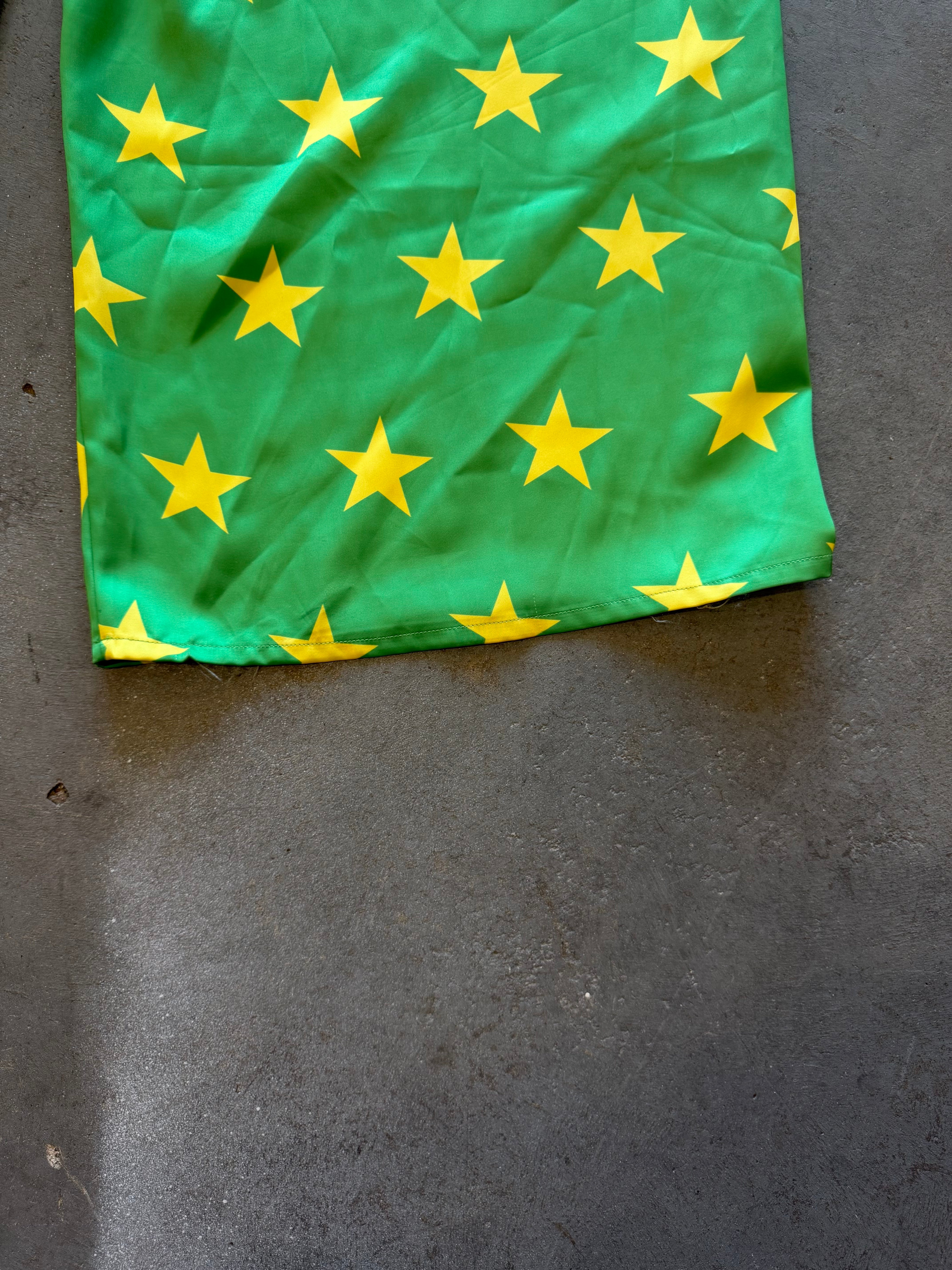A green fabric item, likely a skirt or scarf, featuring a pattern of yellow stars, laid flat on a dark gray concrete floor
