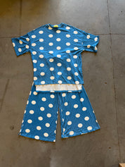 A two-piece short-sleeve pajama set laid flat on a concrete floor, featuring a blue top and matching shorts with a white polka dot pattern