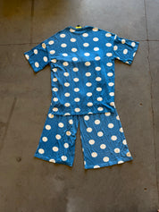 A two-piece short-sleeve pajama set laid flat on a concrete floor, featuring a blue base with a white polka dot pattern