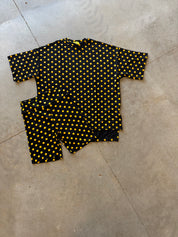 A two-piece biker outfit set consisting of a short-sleeve top and matching pants, featuring a black base with a yellow polka dot pattern, laid flat on a concrete floor