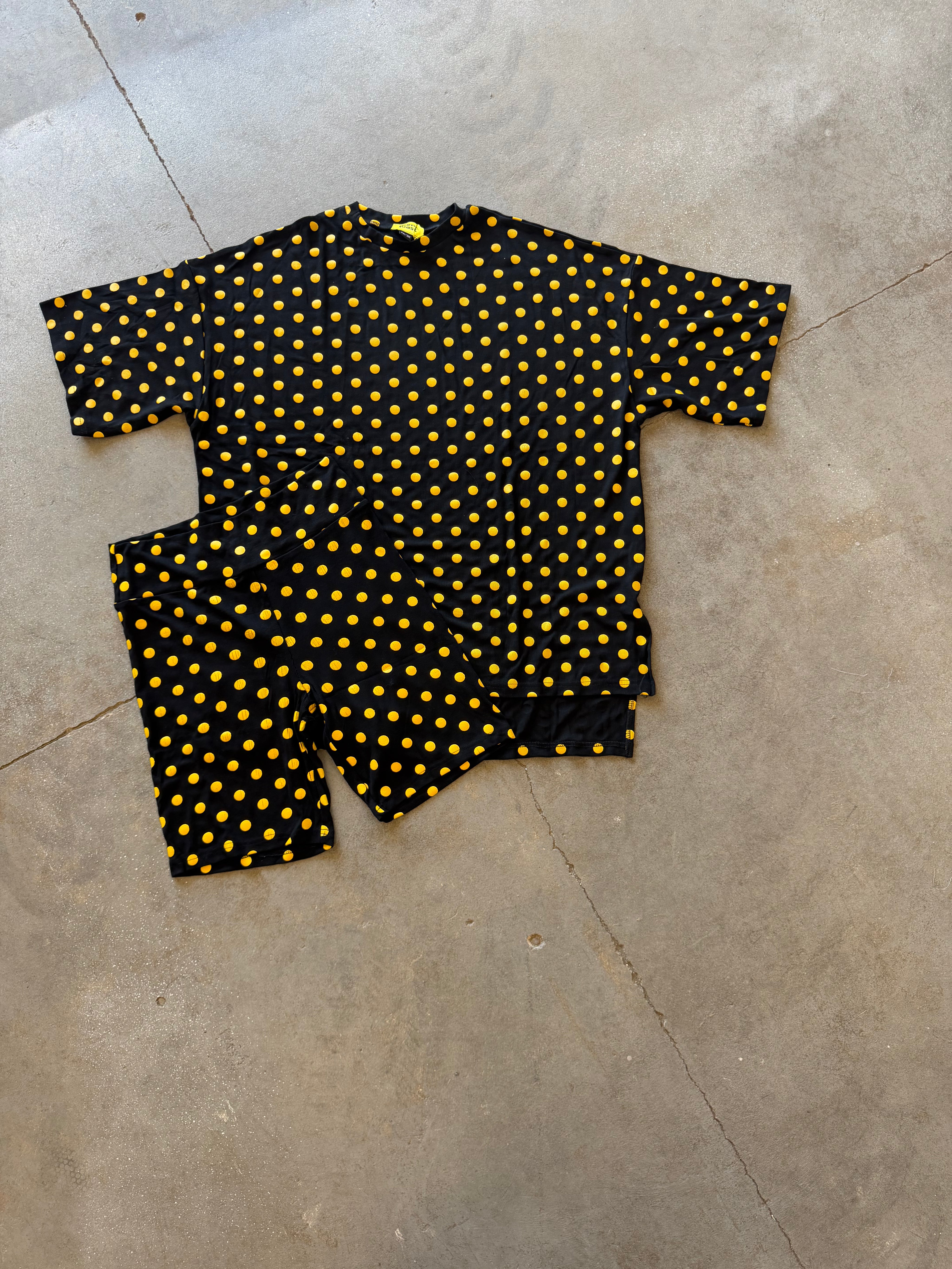 A two-piece biker outfit set consisting of a short-sleeve top and matching pants, featuring a black base with a yellow polka dot pattern, laid flat on a concrete floor