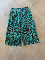 Turquoise and black leopard print shorts laid flat on a beige concrete floor