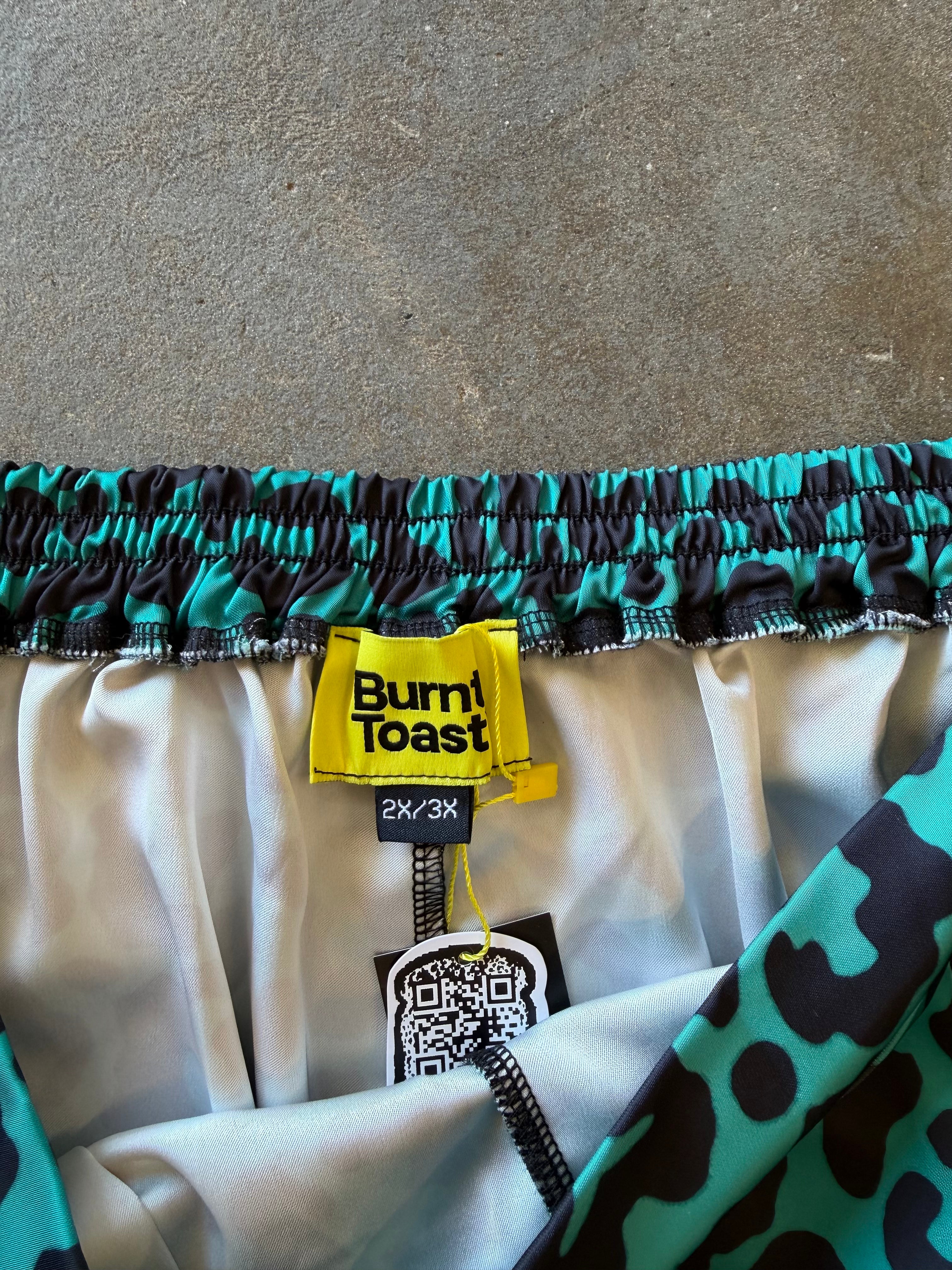 Close-up of a pair of shorts showing the elastic waistband with a black and teal pattern, a yellow Burn! Toast brand label, and a white satin inner lining