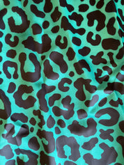 A close-up of a leopard print fabric featuring a bright turquoise green background with dark brown irregular spots